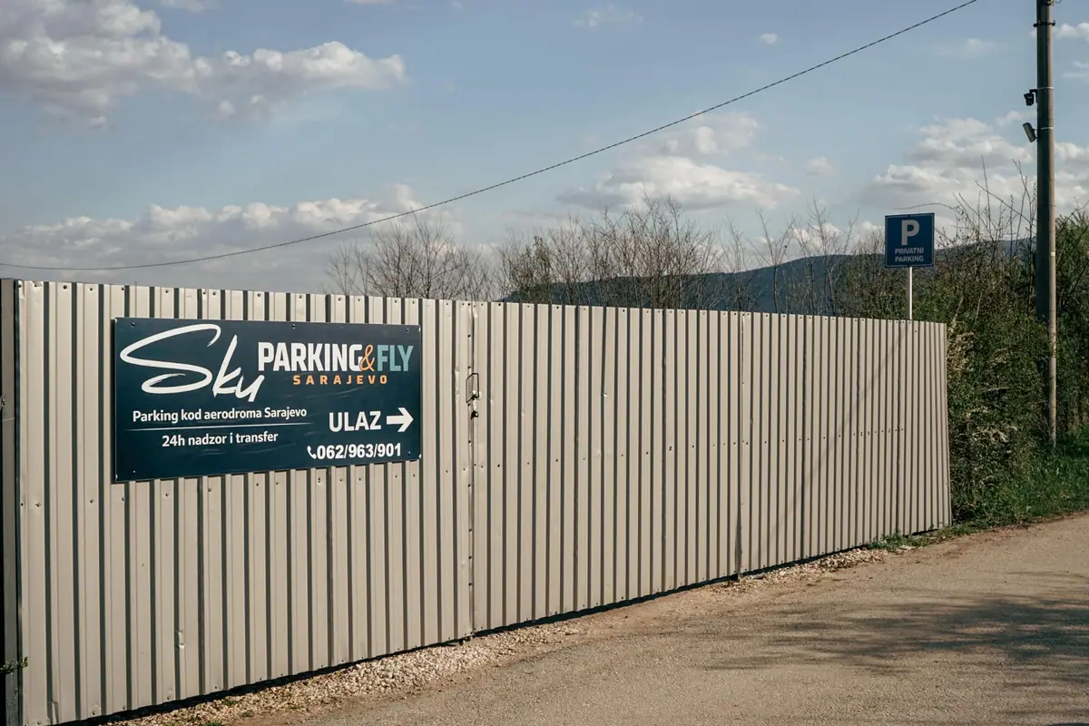 Ulaz na parking: siva limena ograda s tablom Sky Parking & Fly i strelicom ULAZ, plava oznaka Privatni parking i stub s video nadzornom kamerom