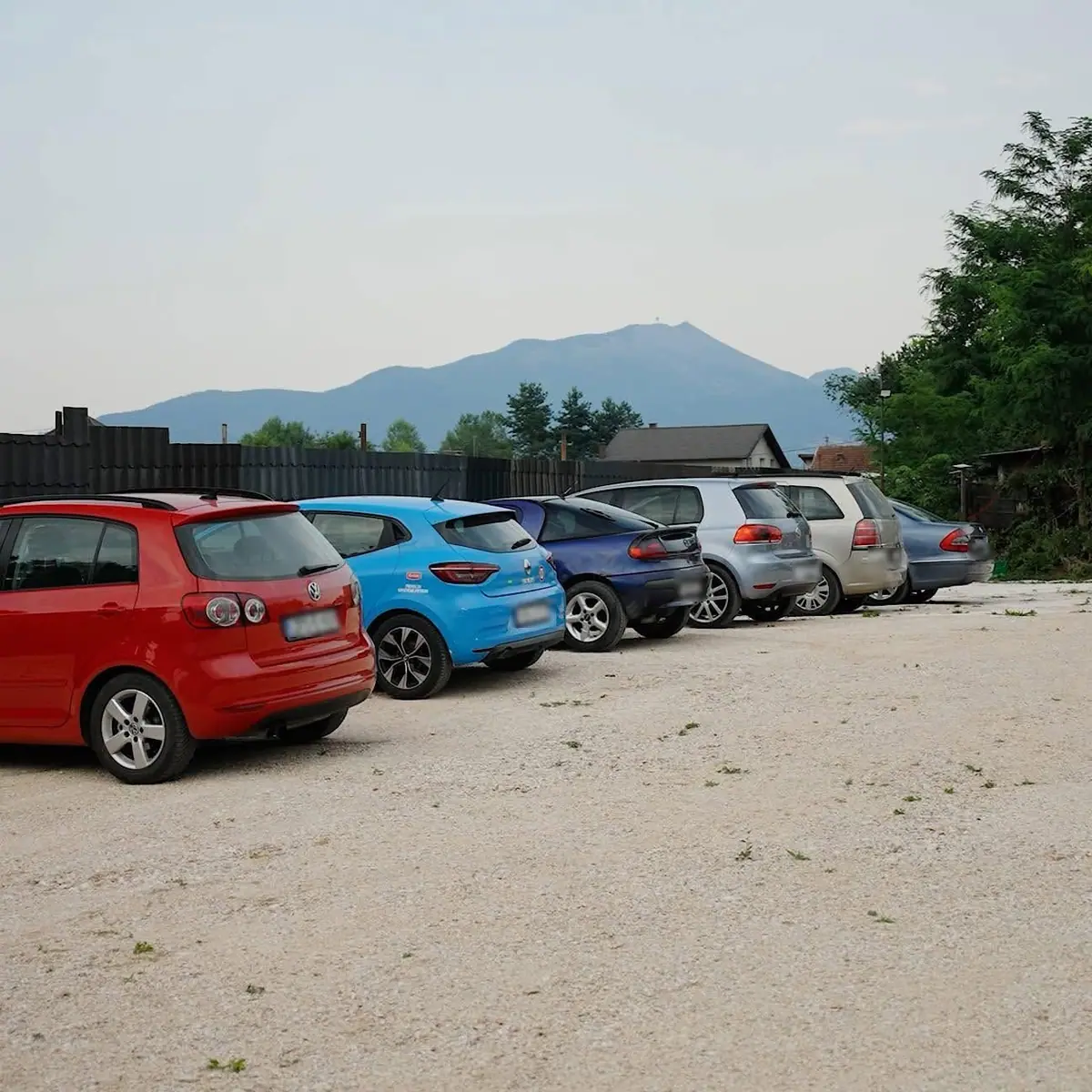 Automobili parkirani u nizu na šljunčanom parkingu, u pozadini planina